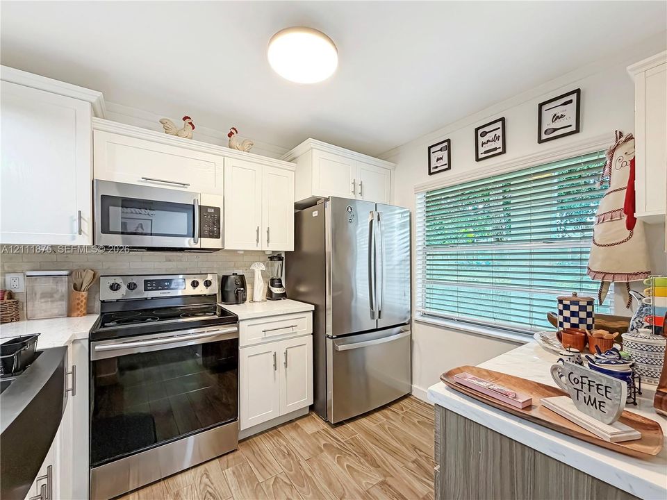 Kitchen featuring white shaker-style cabinetry, wood-finish flooring, stainless steel appliances, and solid surface countertops with a tiled backsplash