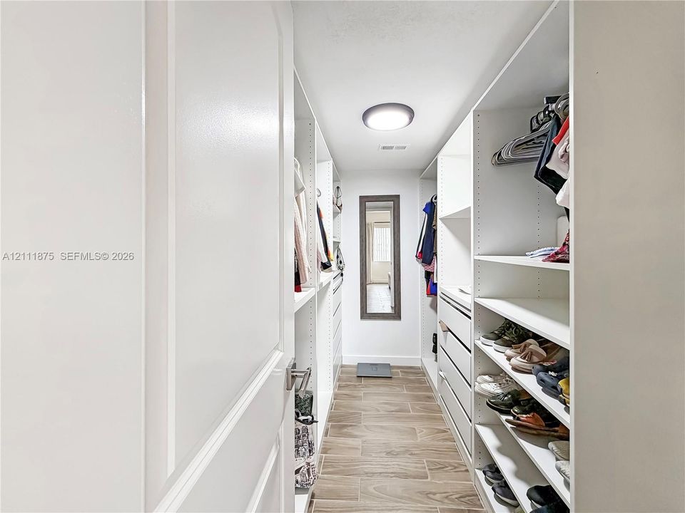 Walk-in closet featuring white built-in shelving, integrated dresser drawers, wood-finish tile flooring, and flush-mount ceiling lighting