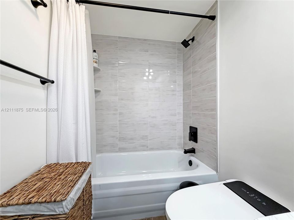 Full bathtub with wall-mounted matte black fixtures and horizontal light-toned ceramic tile surround