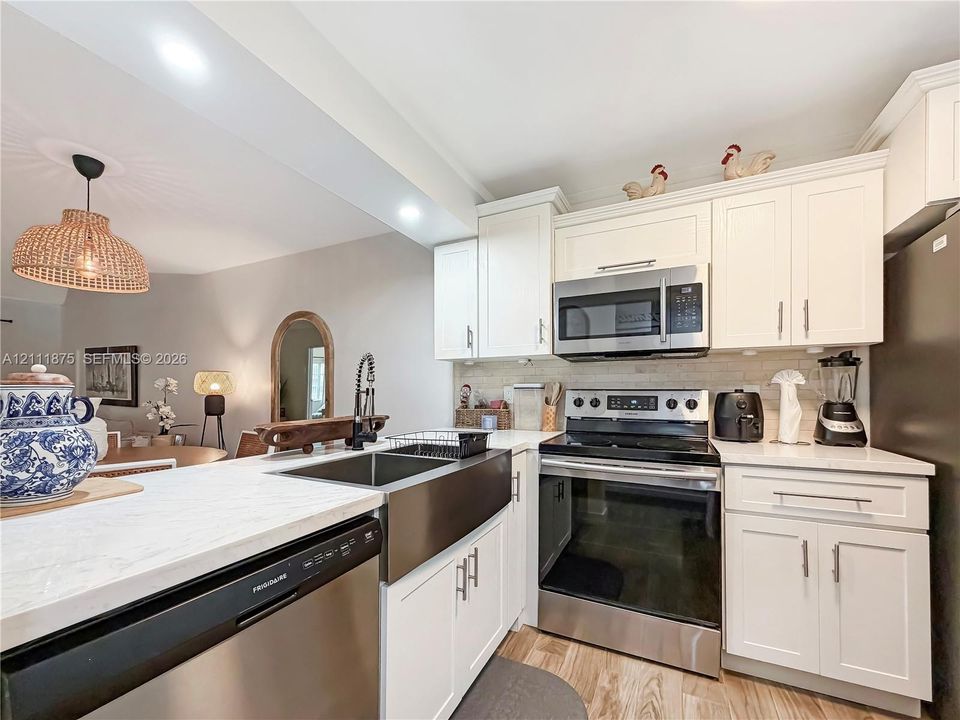 Kitchen featuring white cabinetry, stainless steel appliances, a farmhouse-style sink, stone-finish countertops, and wood-finish flooring