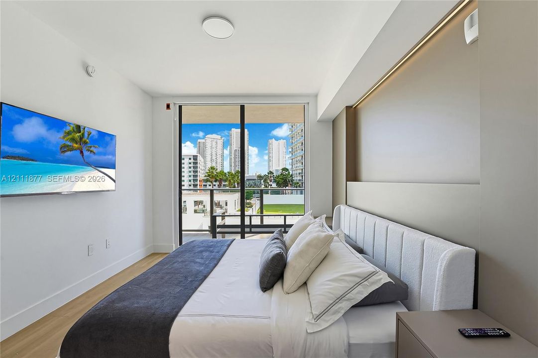 Floor-to-ceiling glass sliding doors opening to a balcony, light-toned wood-finish flooring, recessed linear accent lighting, and neutral wall tones