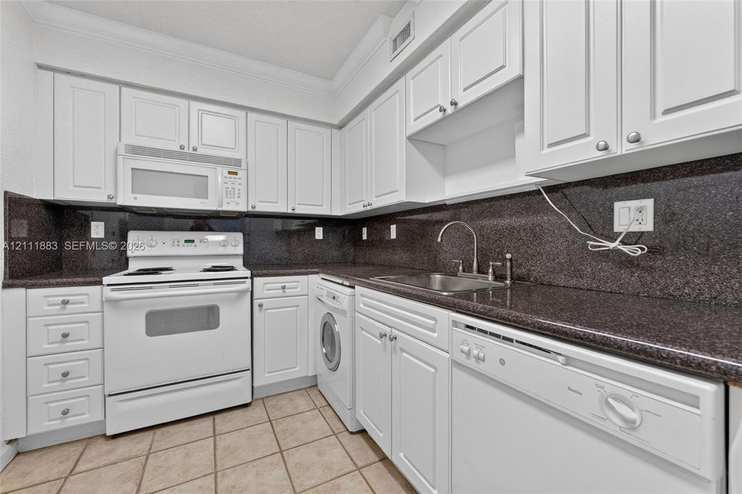 Kitchen featuring white cabinetry, dark stone-finish countertops, stainless steel sink with gooseneck faucet, built-in white appliances, and tile flooring