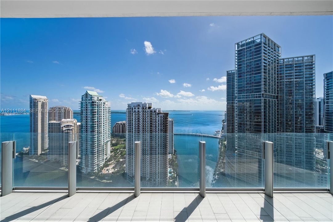 Covered balcony featuring tile flooring and a glass panel railing, showcasing an expansive waterfront and city skyline panorama