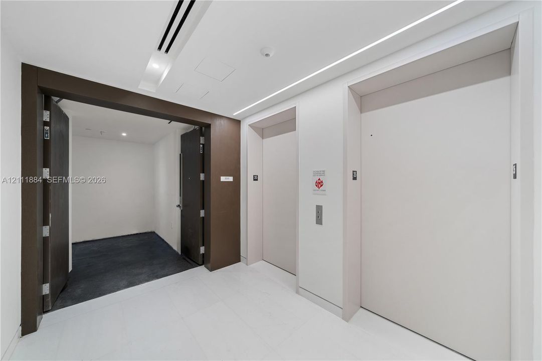 Elevator landing featuring dual elevator doors, stone flooring, recessed ceiling lighting, and a dark wood-finish entryway frame