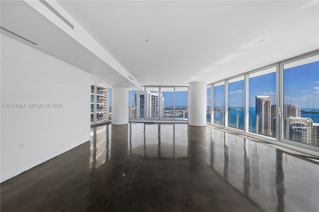 Expansive open-concept interior featuring polished concrete flooring, floor-to-ceiling glass windows, and panoramic water and urban skylines
