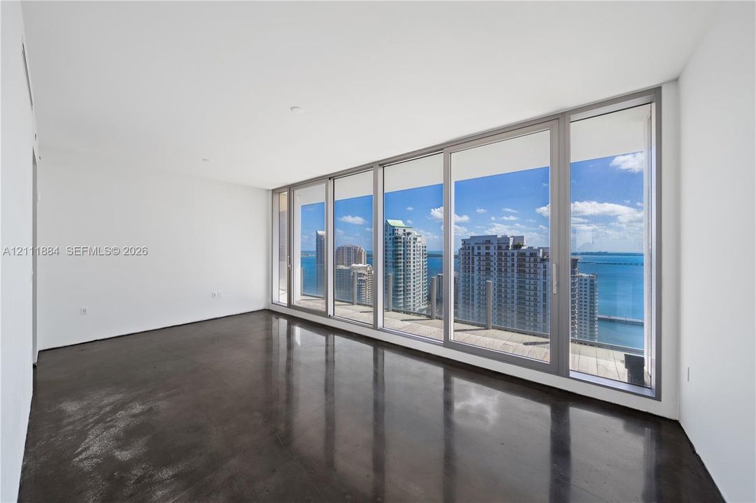 Floor-to-ceiling windows, polished concrete flooring, recessed lighting, and a glass-railed balcony with a coastal skyline backdrop