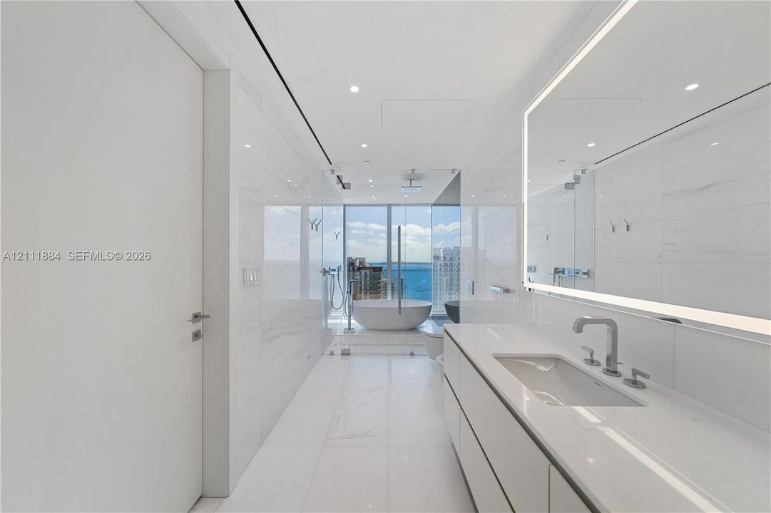 Modern bathroom featuring floor-to-ceiling tiled walls, a floating vanity with a seamless countertop, a large illuminated vanity mirror, a glass-enclosed shower, and a freestanding soaking tub