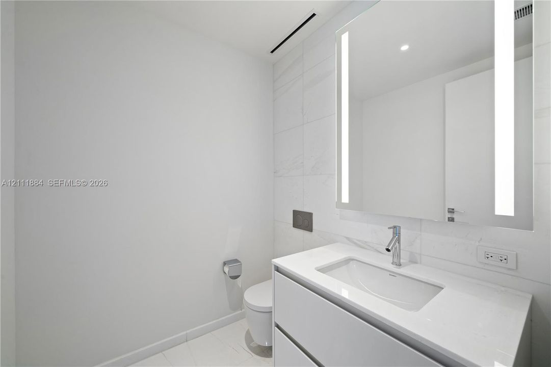 Floating vanity featuring a white countertop and rectangular basin, integrated LED-backlit mirror, wall-mounted faucet, and large-format tile wall