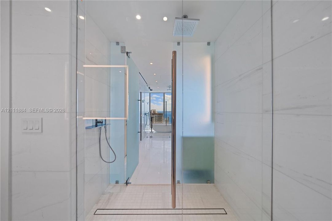 Walk-in shower featuring floor-to-ceiling tiled walls, frameless glass door, ceiling-mounted rainfall showerhead, handheld shower fixture, and linear drain
