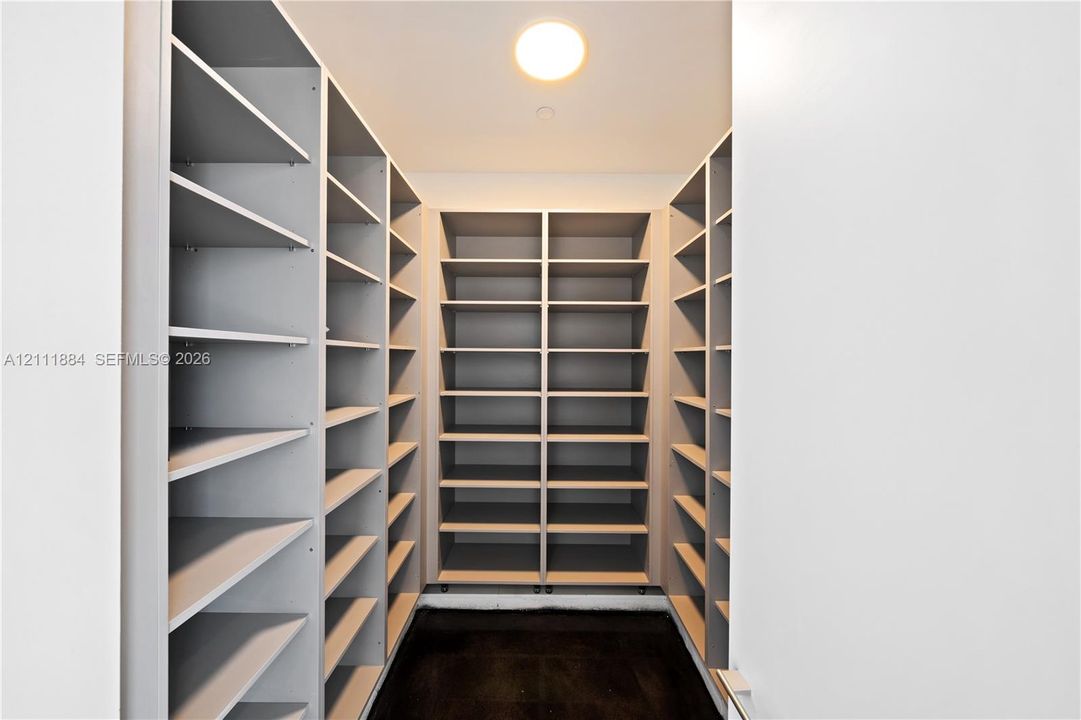 Walk-in storage area featuring custom floor-to-ceiling built-in cabinetry with extensive shelving, neutral finish, and recessed ceiling lighting