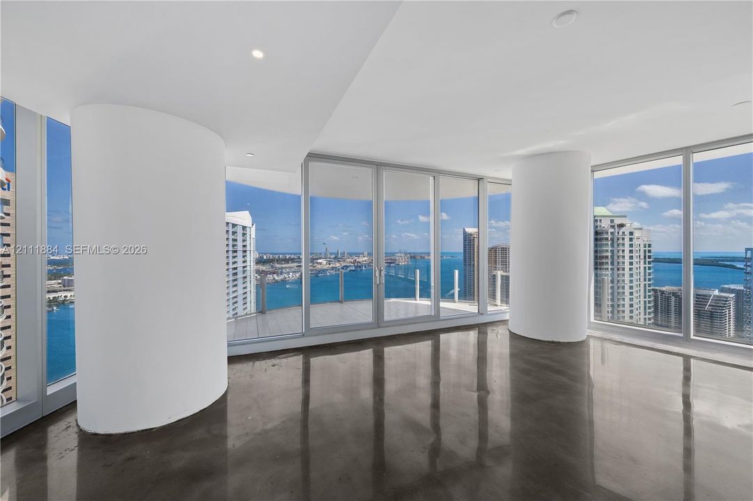 Floor-to-ceiling glass walls, polished concrete flooring, rounded structural columns, recessed lighting, and integrated balcony access