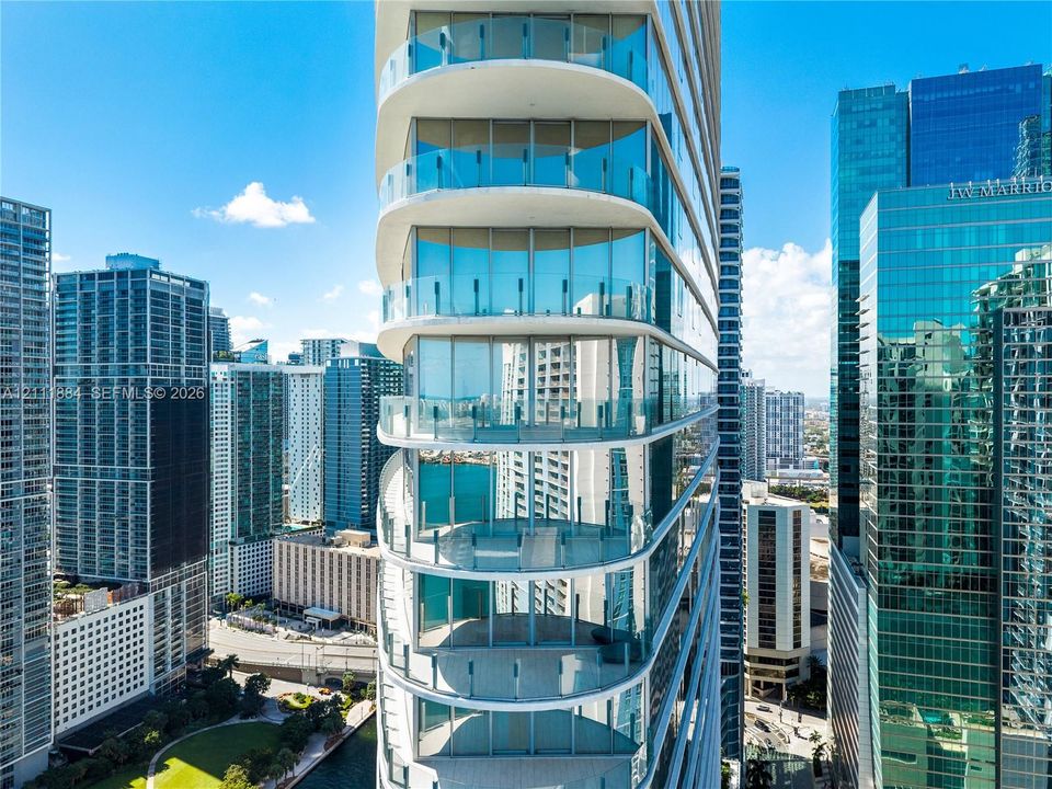 High-rise architectural exterior featuring tiered, curved structural design, floor-to-ceiling glass wall systems, and wrap-around glass panel balcony railings