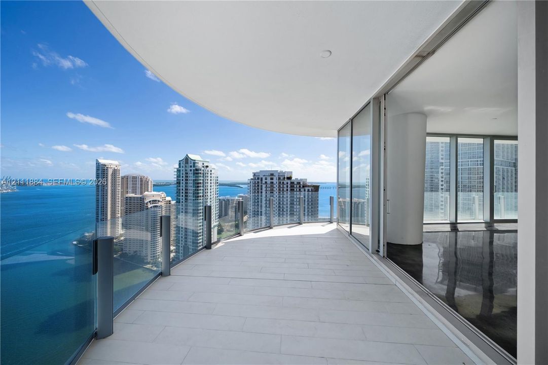 Wraparound balcony featuring large-format tile flooring, a glass panel railing, and expansive floor-to-ceiling glass sliding doors