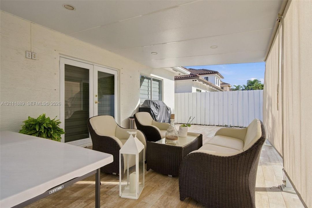 Covered patio featuring wood-finish tile flooring, recessed lighting, and a white privacy fence