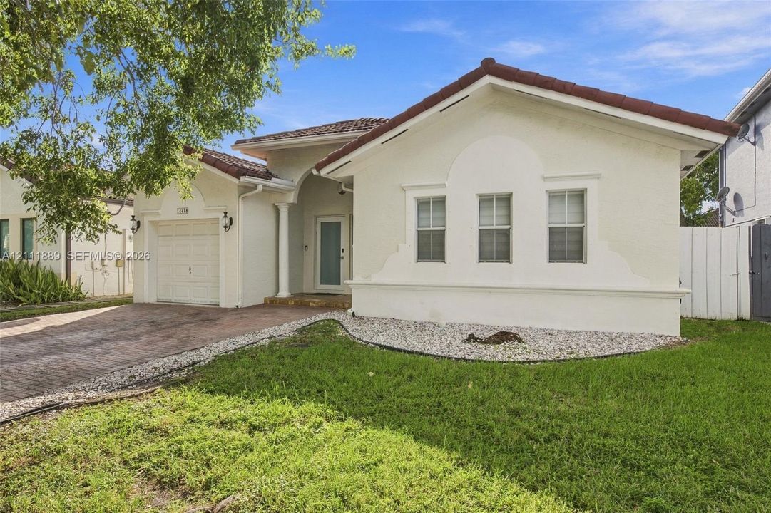 Stucco exterior featuring arched architectural detailing, tile roof, brick-paver driveway, and a covered entryway with a decorative column