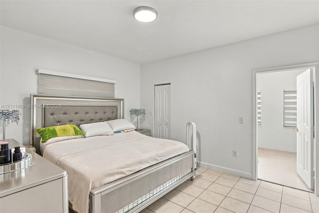 Bedroom featuring neutral wall paint, tile flooring, dual-panel closet doors, and layered window blinds