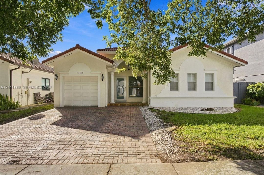 Stucco exterior featuring decorative arched trim, a brick-paver driveway, a single-car garage, and a covered entryway with column detailing