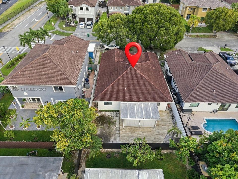 Aerial perspective of residential property featuring a hipped tile roof, stone-finish patio, covered pergola, and partial perimeter fencing