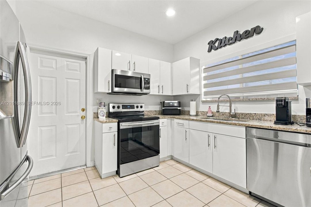 Kitchen featuring white cabinetry, stone-finish countertops, stainless steel appliances, tile flooring, and a recessed sink with a high-arch faucet