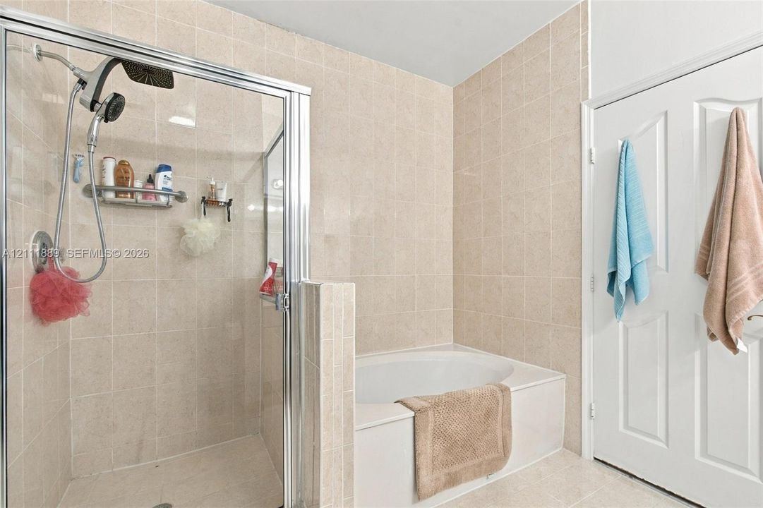 Walk-in shower with a glass enclosure, built-in tile surround, and a multi-function shower head, featuring a deep soaking tub with a tiled surround