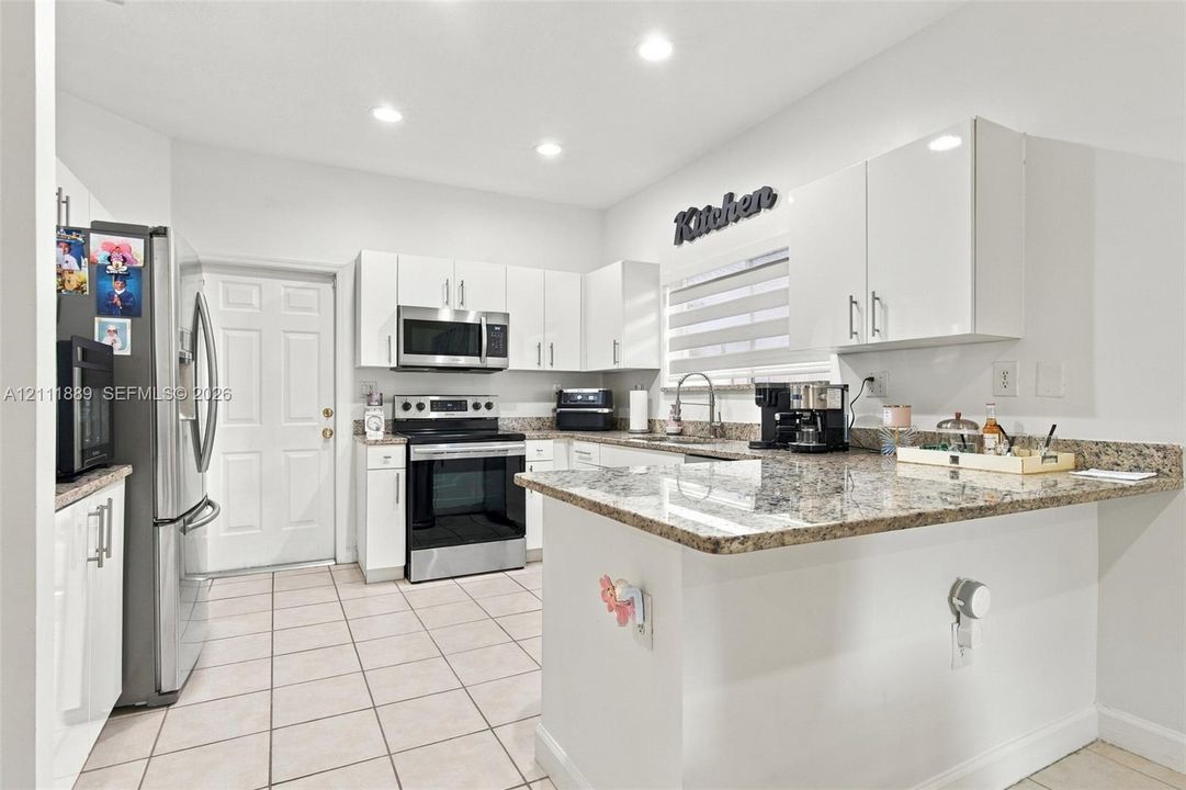 Kitchen featuring white flat-panel cabinetry, stone-finish countertops, stainless steel appliances, recessed ceiling lighting, and tile flooring