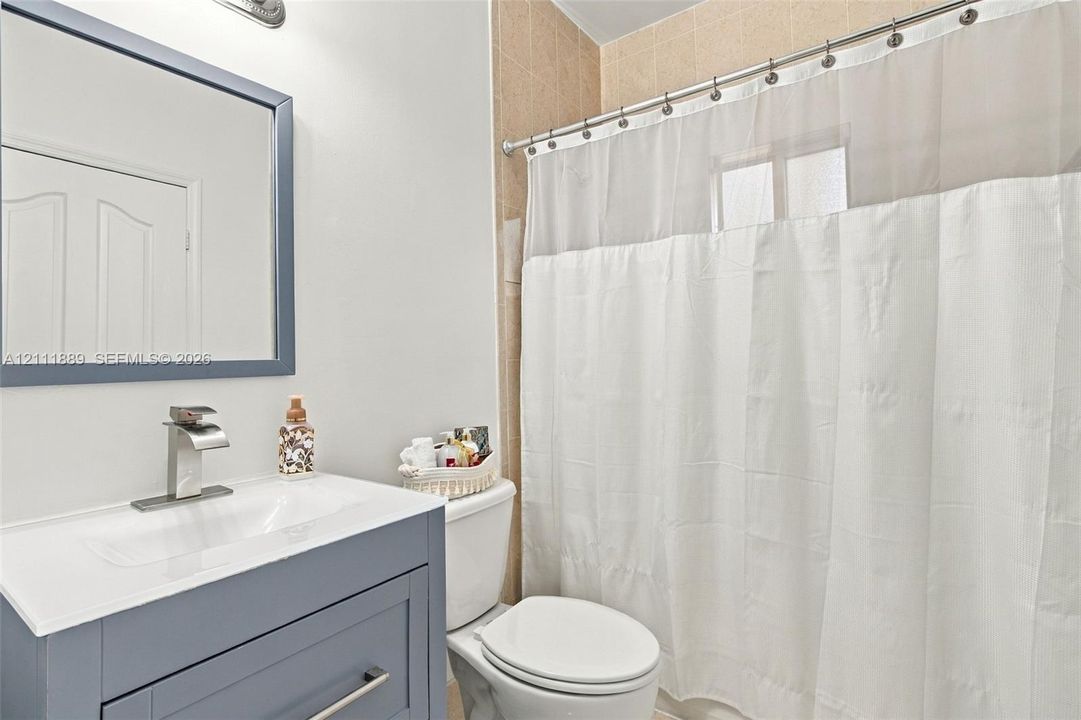 Blue vanity featuring a white countertop with an integrated basin, a polished chrome single-handle faucet, a framed mirror, and a tiled shower surround