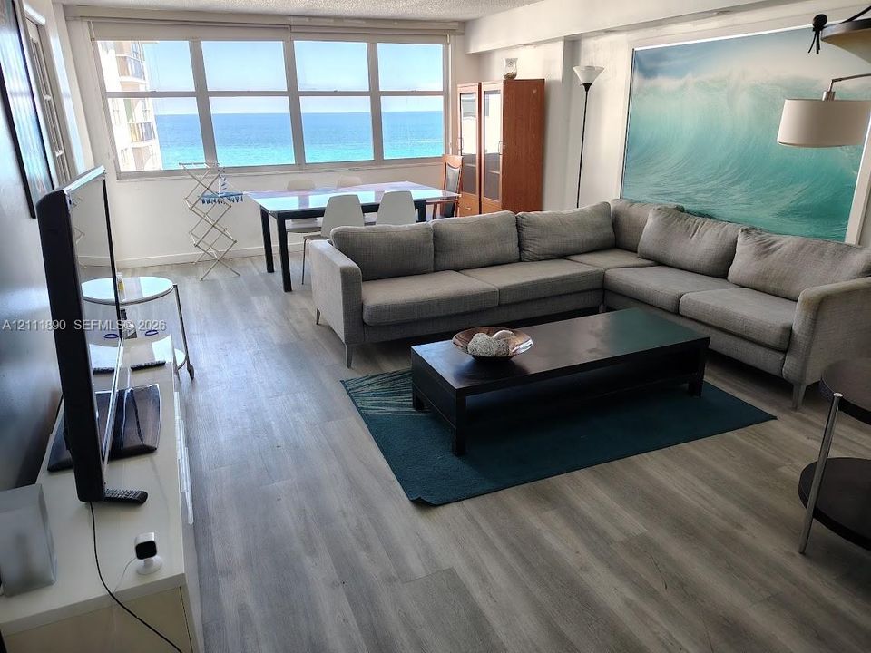 Open-concept living space featuring wood-finish flooring and a expansive wall of windows with an ocean backdrop