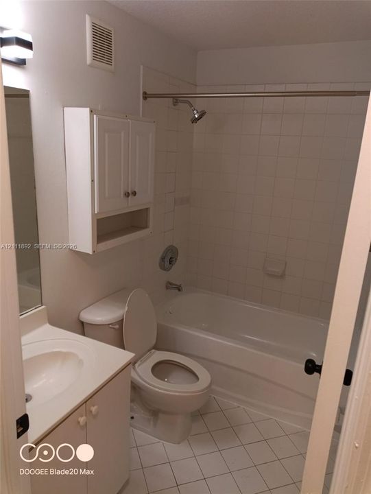 Bathroom featuring a tub and shower combination with full-height tile surround, wall-mounted white cabinetry, a single-basin vanity, and tiled flooring