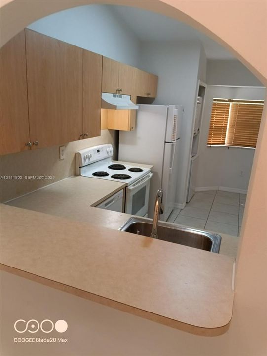 Kitchen featuring flat-panel wood-finish cabinetry, solid-surface countertops, a stainless steel undermount sink, and tile flooring