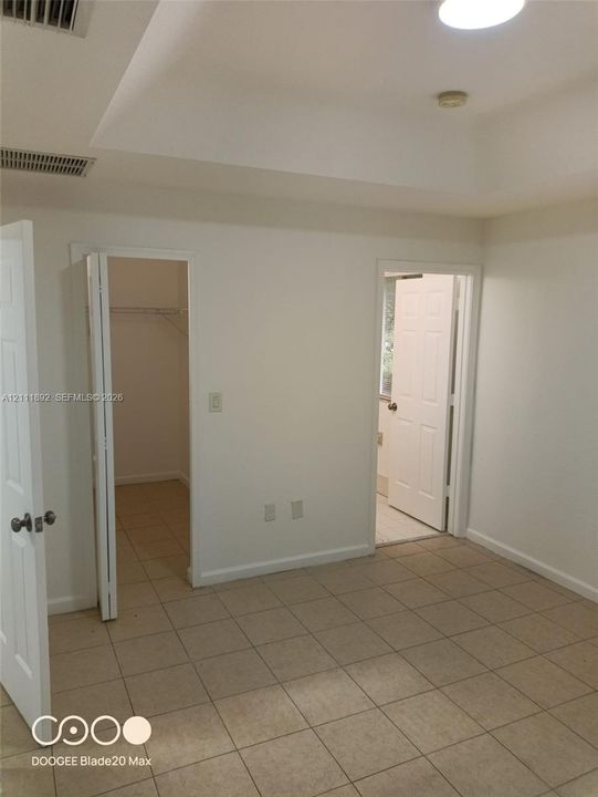 Room featuring a tray ceiling, tile flooring, walk-in closet with built-in shelving, and multiple six-panel interior doors