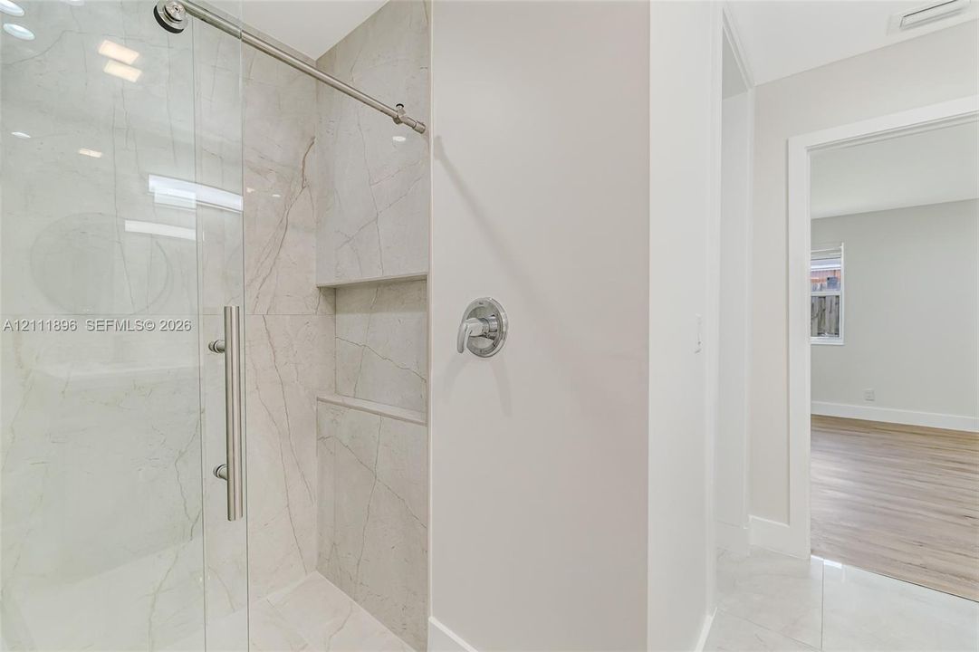 Walk-in shower featuring large-format stone-finish tile surround, a built-in recessed niche, chrome hardware, and a frameless glass enclosure