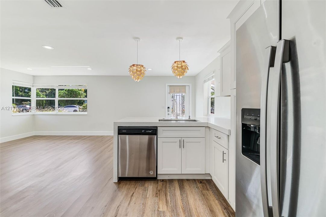 Kitchen featuring white cabinetry, stainless steel appliances, wood-finish flooring, stone-style countertops, and pendant lighting
