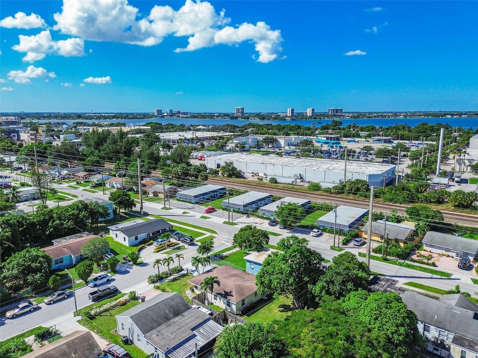 Aerial perspective of the property featuring mature landscaping, residential street access, and a backdrop of regional water and cityscape