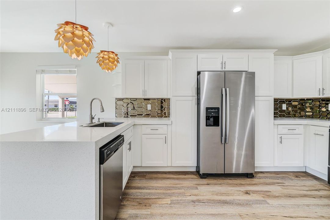 Kitchen featuring white cabinetry, solid-surface countertops, stainless steel appliances, geometric-patterned backsplash, and wood-finish flooring