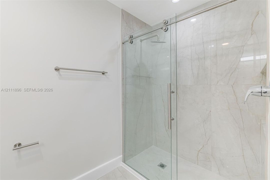 Walk-in shower featuring large-format tile surround, frameless glass sliding door, rainfall showerhead, and wall-mounted brushed metal fixtures