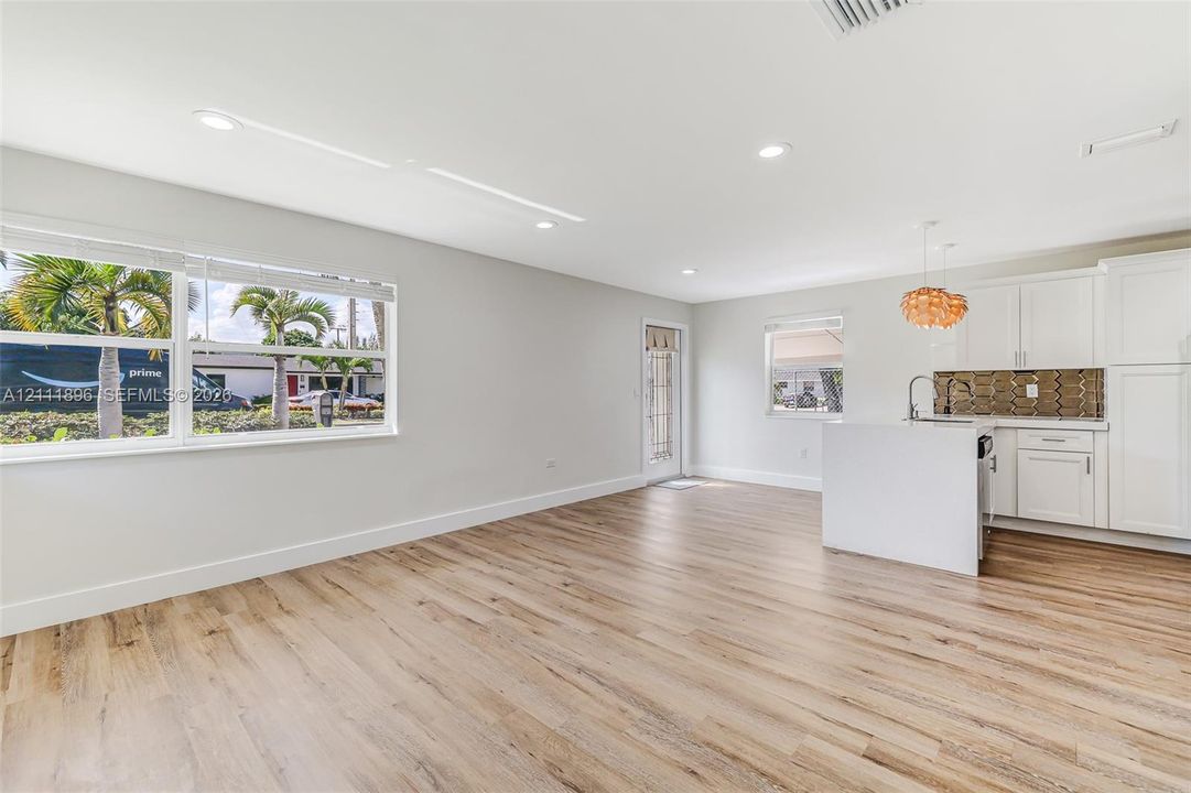 Open-concept living space featuring wood-finish flooring, recessed lighting, white cabinetry, a kitchen island with a built-in sink, and a decorative tile backsplash