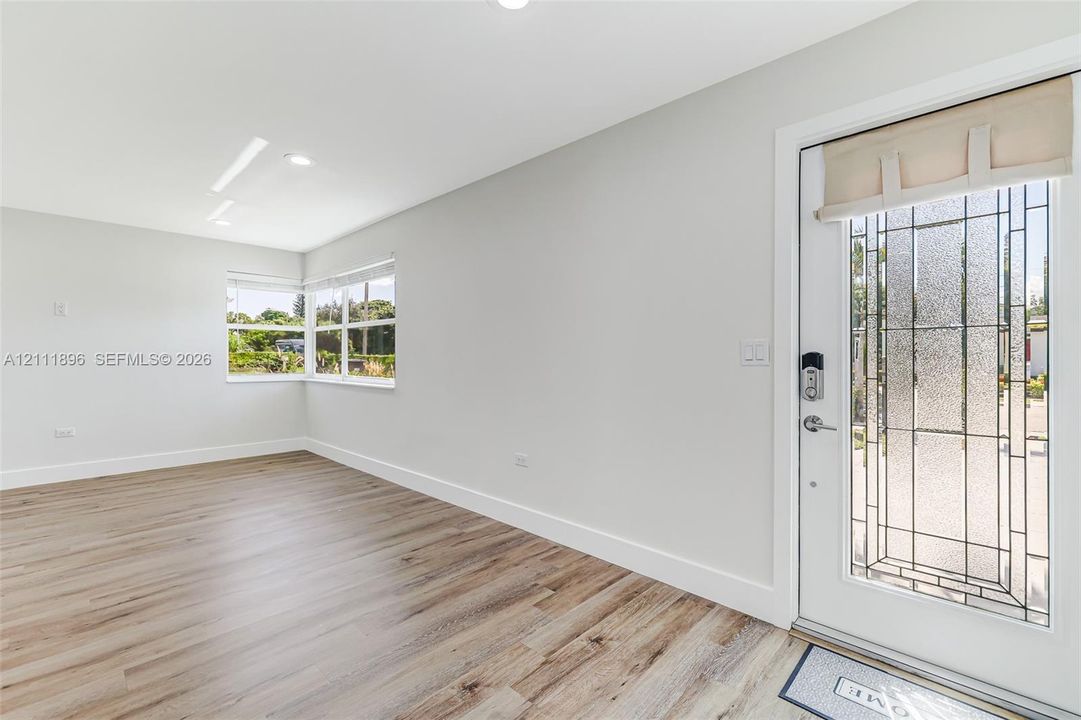 Neutral-toned interior featuring wood-finish flooring, recessed lighting, and a front entry door with a decorative glass insert