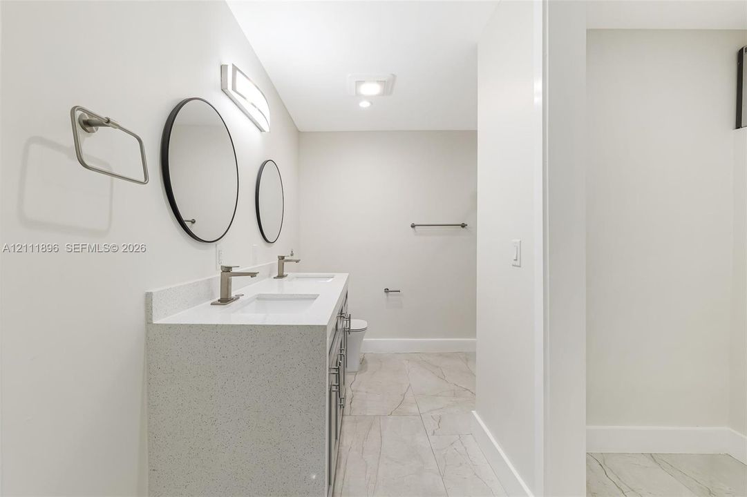Double vanity featuring a light-toned countertop, rectangular undermount sinks, and wall-mounted circular mirrors