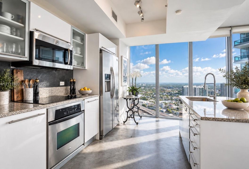 Kitchen featuring white cabinetry with glass-front uppers, stainless steel appliances, stone countertops, a center island with an integrated sink, and floor-to-ceiling windows