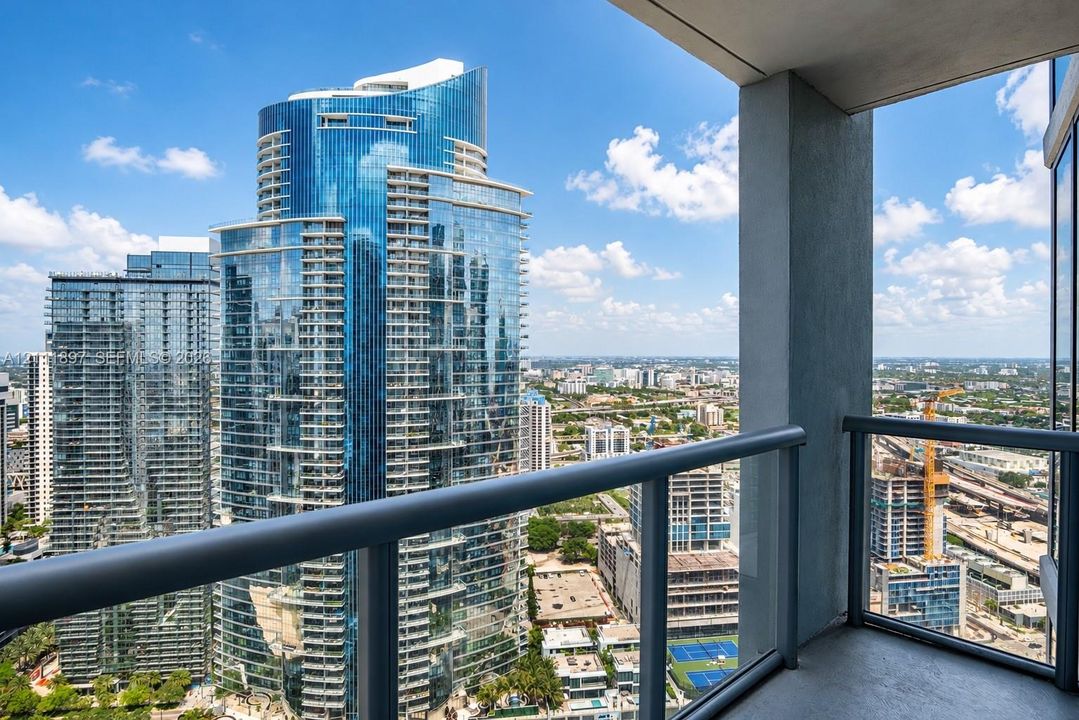 Private balcony featuring metal railings with glass panels, concrete flooring, and an elevated cityscape perspective