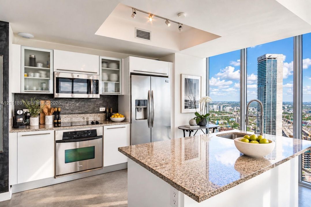 Kitchen featuring white cabinetry, stone countertops, stainless steel appliances, a central island with a built-in sink, and floor-to-ceiling windows