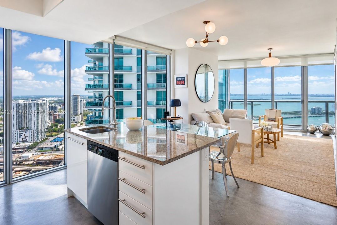 Kitchen featuring a stone countertop island, stainless steel dishwasher, and under-mount sink, complemented by floor-to-ceiling windows and modern multi-light fixtures