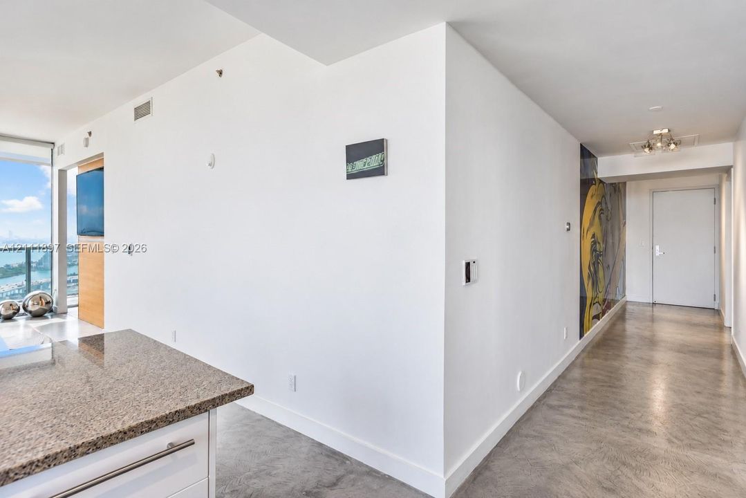 Polished concrete flooring throughout, stone-surface kitchen peninsula, floor-to-ceiling glass wall, and decorative wall mural
