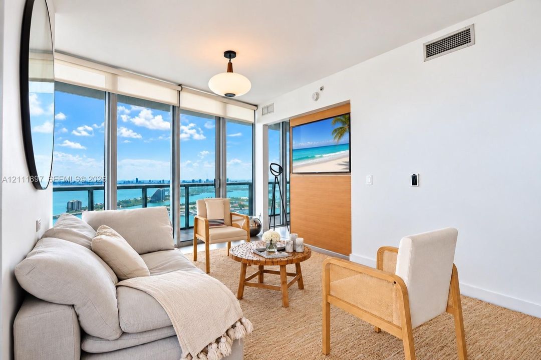 Floor-to-ceiling glass wall, recessed lighting, wood-finish wall paneling, and a private balcony overlooking the water