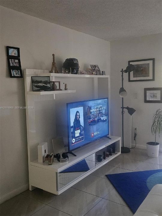 Built-in white entertainment center featuring a high-gloss finish, mirrored drawer fronts, and open display shelving, paired with tile flooring