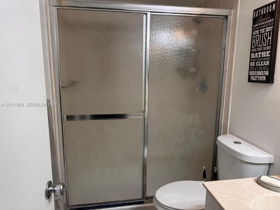 Shower enclosure featuring chrome-finish sliding doors and textured glass, tile surround, and a standard-height toilet
