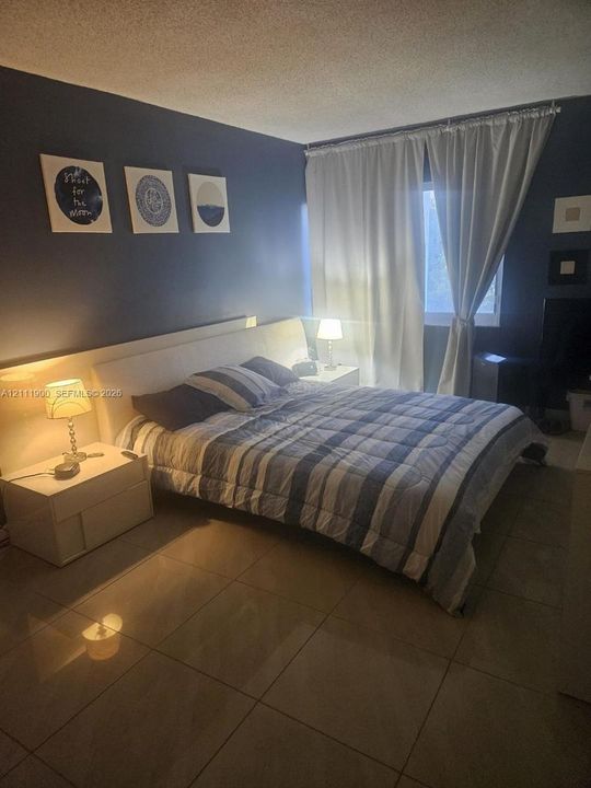 Room featuring large-format tile flooring and a window with floor-to-ceiling drapery