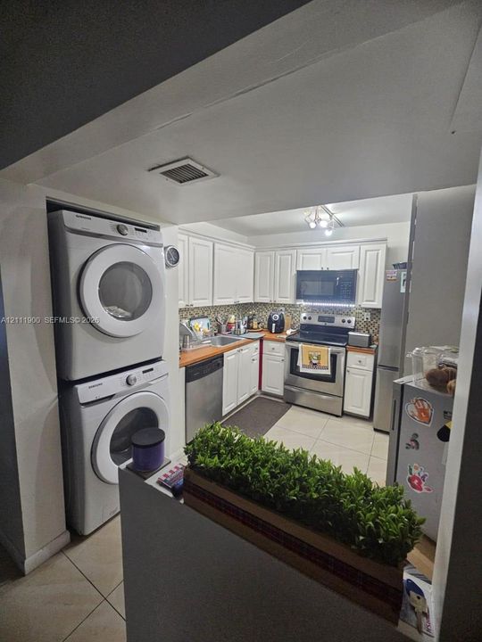 Kitchen featuring white shaker-style cabinetry, stainless steel appliances, tile flooring, and integrated laundry area