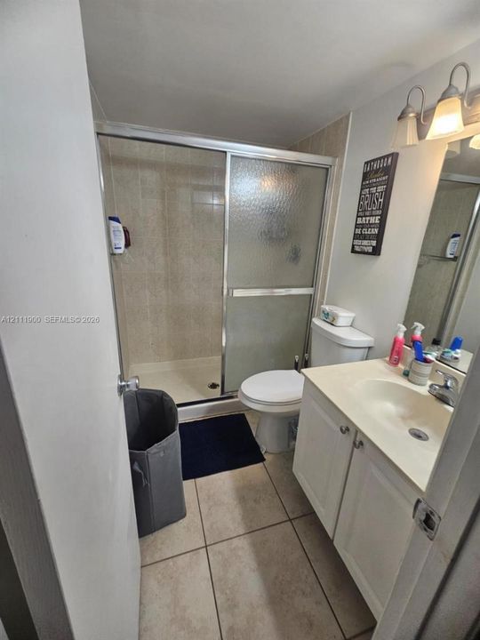 Bathroom featuring a walk-in shower with glass sliding doors, tiled flooring, a white vanity cabinet, and wall-mounted vanity lighting