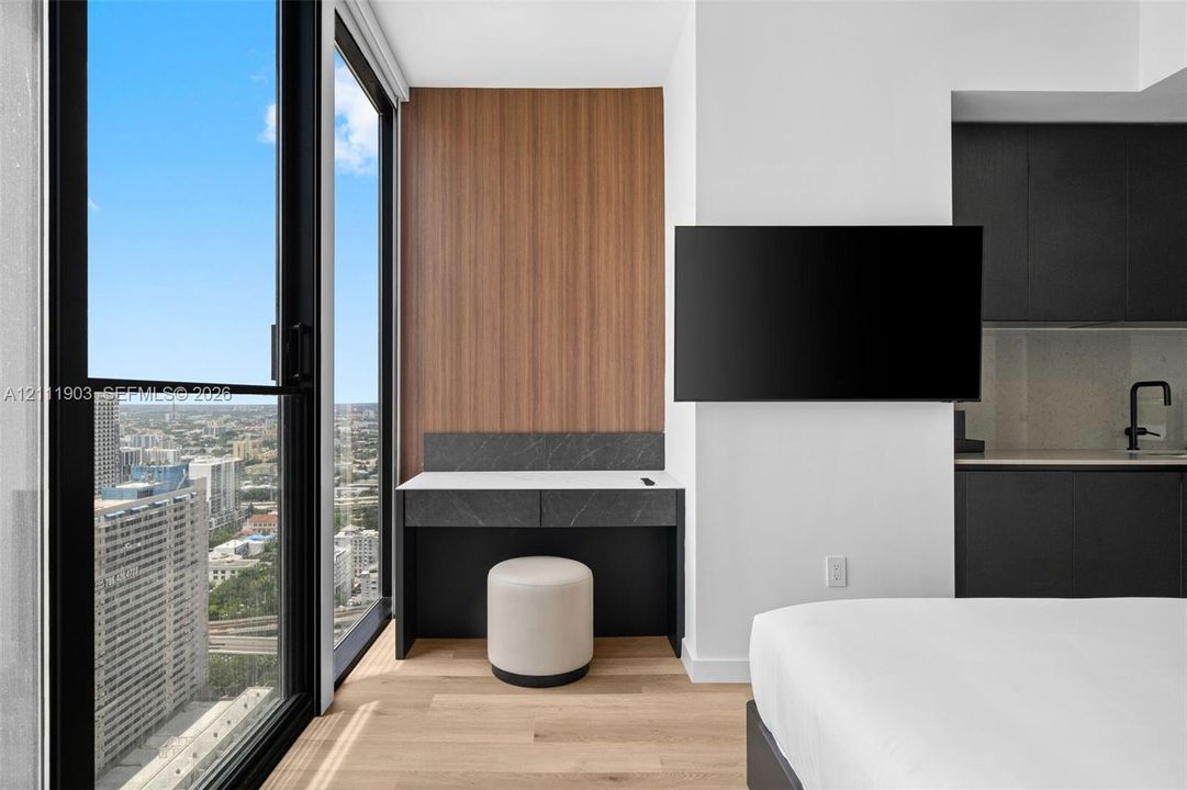 Floor-to-ceiling windows, wood-finish flooring, built-in desk with stone surface, and matte black kitchen fixtures